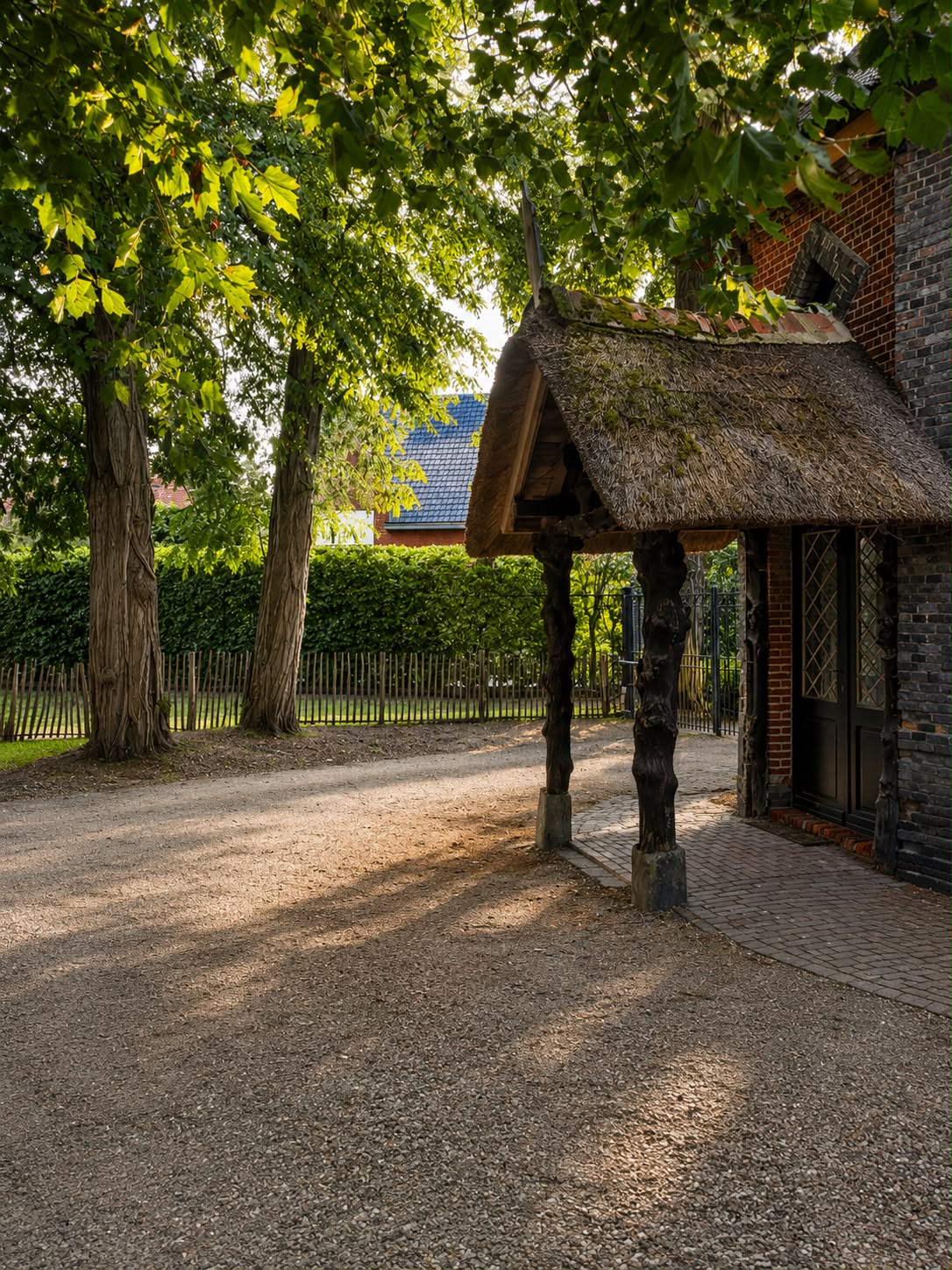 Oprit met bomen en rieten luifel aan de voordeur