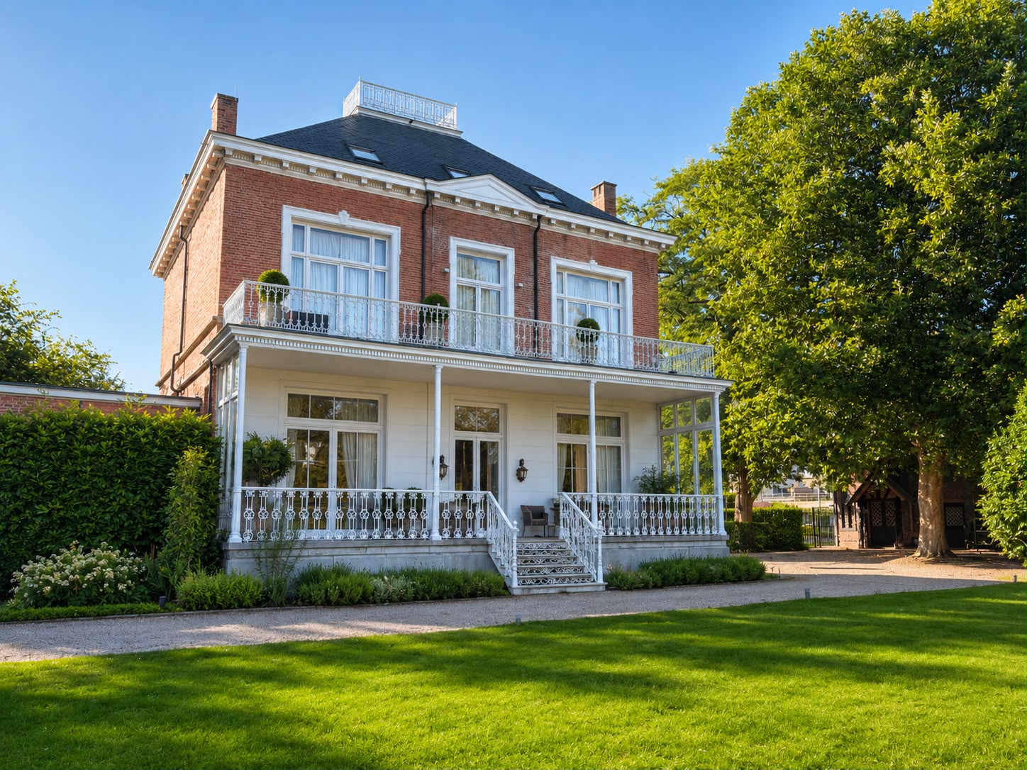 Voorgevel van het herenhuis met witte veranda, smeedijzeren balkon en gazon
